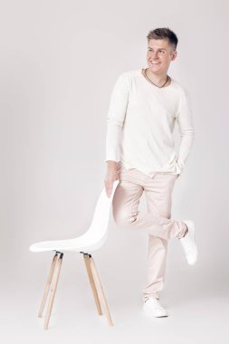 yakışıklı genç adam beyaz kazaklı bir sandalyeye oturur