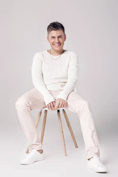 Joven guapo en suéter blanco se sienta en una silla en — Foto de Stock