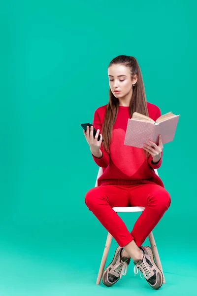 Ragazza legge libro e utilizza smartphone . — Foto Stock