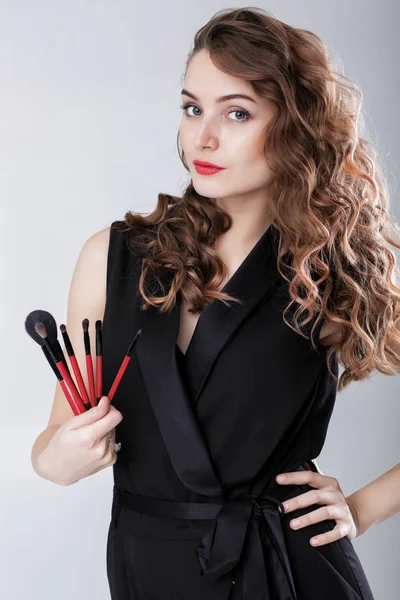 Visagistin mit natürlichem Make-up hält Make-up-Pinsel auf grauem Hintergrund — Stockfoto
