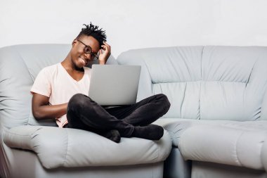 Kanepe üstünde laptop ile oturan gözlüklü adam