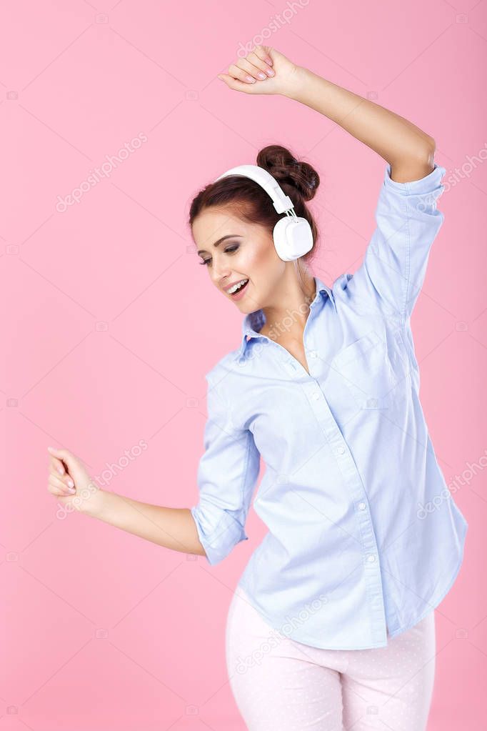 Beautiful woman in headphones enjoying listening to music and dancing on pink background