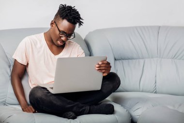 Kanepe üstünde laptop ile oturan gözlüklü adam