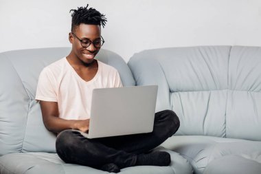 Kanepe üstünde laptop ile oturan gözlüklü adam