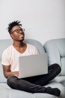 Kanepe üstünde laptop ile oturan gözlüklü adam