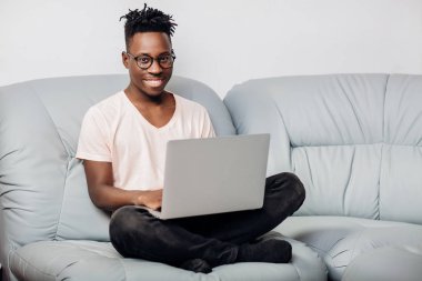 Kanepe üstünde laptop ile oturan gözlüklü adam