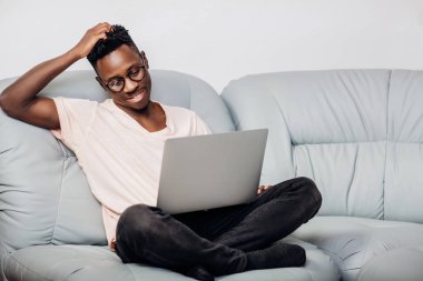 Kanepe üstünde laptop ile oturan gözlüklü adam