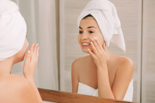 Mujer aplicando crema en su cara en el baño — Foto de Stock