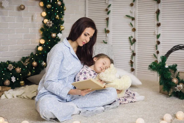 Мати читає книгу своїй маленькій милій доньці біля ялинки — стокове фото