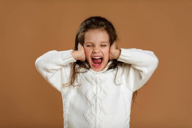 Cute curly little girl in white sweater is closing her ears clipart