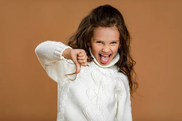 Dziecko dziewczyna w białym swetrze pokazując kciuki w dół — Zdjęcie stockowe