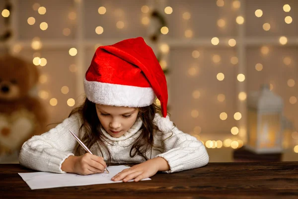 Menina em santa chapéu escrevendo carta para Papai Noel — Fotografia de Stock