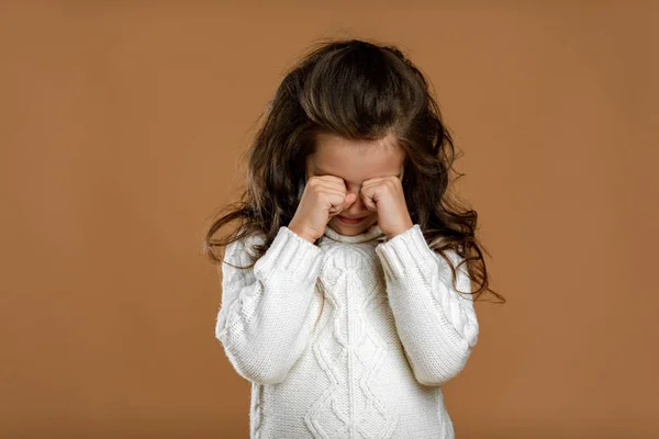Rozrušený kudrnaté malé dítě dívka v bílém svetru na béžovém pozadí. — Stock fotografie