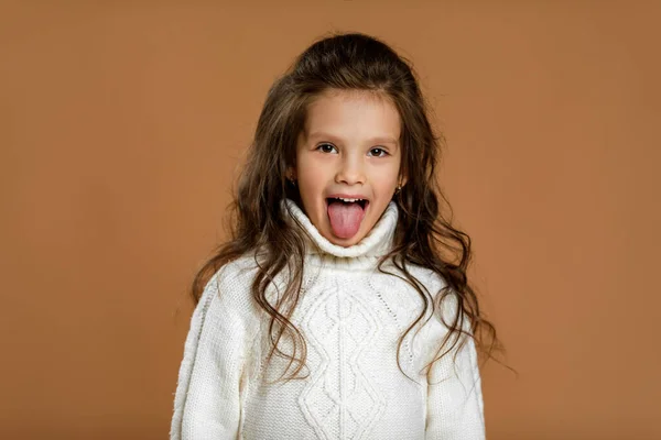 Маленька дівчинка в білому светрі показує язик — стокове фото