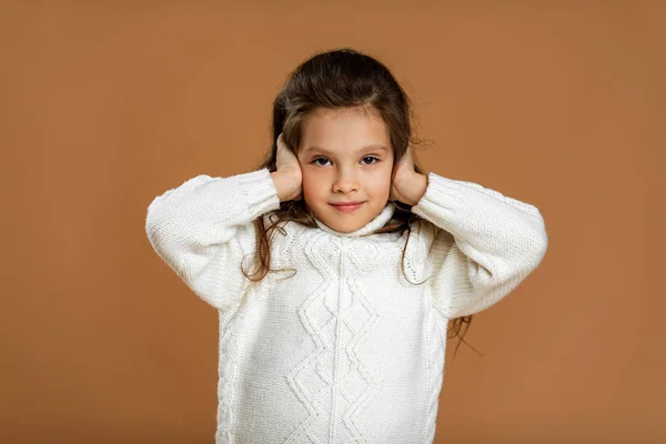 Симпатична кучерява дівчинка в білому светрі закриває вуха — стокове фото