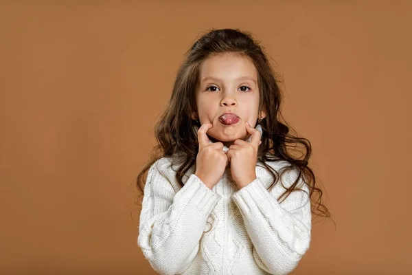 Niña pequeña en suéter blanco mostrando su lengua — Foto de Stock