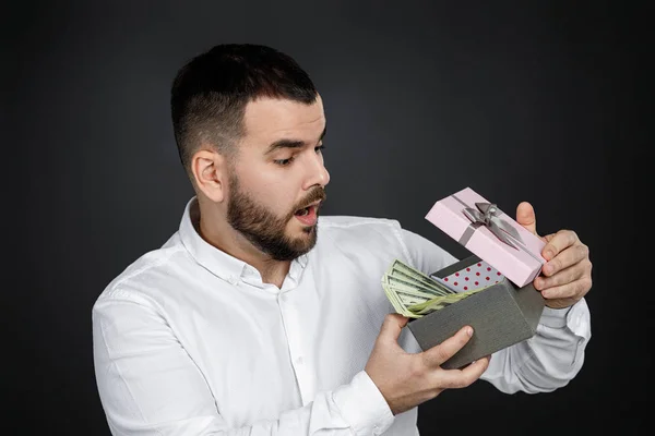 Portré jóképű szakállas férfi fehér ingben kinyitja ajándék doboz pénzzel — Stock Fotó