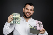 portrét pohledného vousatého muže v bílé košili otevírá dárkovou krabici s penězi