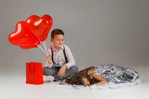 Enfant garçon tient rouge coeur en forme de ballons et fille se trouve à proximité — Photo