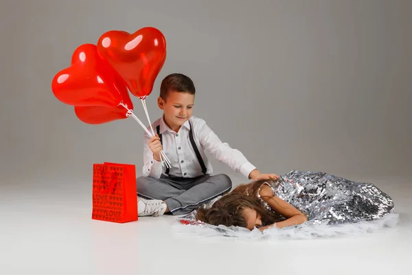 Niño niño sostiene rojo corazón en forma de globos y chica se encuentra cerca — Foto de Stock