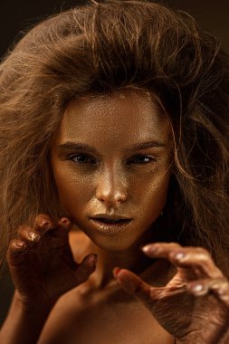 beaty woman with gold metallic body and hair on dark background.
