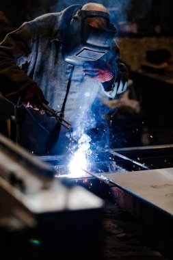 Koruyucu üniformalı ve kaynak metalini maskeli işçiler.