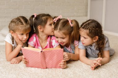 Bir grup çocuk yere yatıp masal kitabı okuyor.