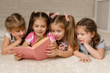 Bir grup çocuk yere yatıp masal kitabı okuyor.