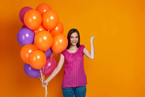 Дівчина з яскравими різнокольоровими повітряними кульками піднімає згорнуті кулаки — стокове фото