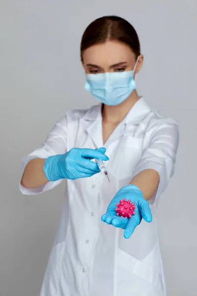 Woman doctor in mask and rubber gloves holding syringe and virus model — Stock Photo, Image