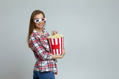 Kırmızı-mavi gözlüklü gülümseyen kadın elinde patlamış mısır kovası tutuyor.