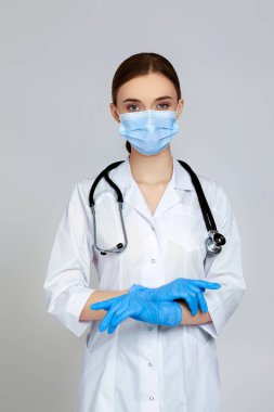 Beyaz önlüklü ve steteskoplu güzel kadın doktor portresi gri arka planda izole edilmiş.