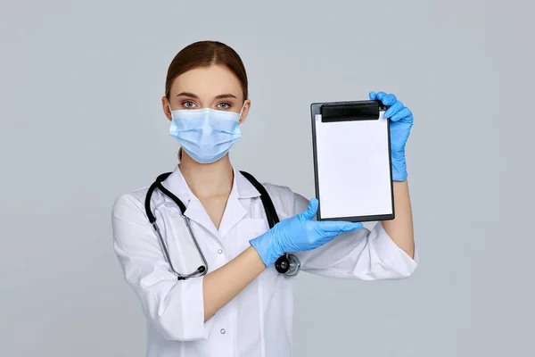 Kvinna läkare i mask och gummihandskar och med stetoskop hålla urklipp — Stockfoto
