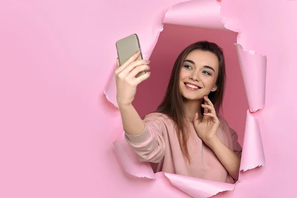 Κορίτσι κρατώντας έξυπνο τηλέφωνο στο χέρι σε σχισμένο χαρτί ροζ τοίχο — Φωτογραφία Αρχείου