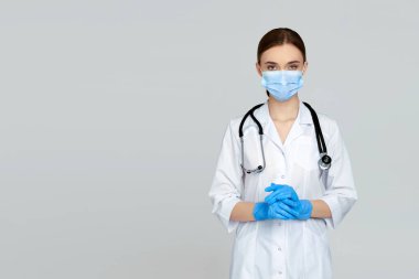 Beyaz önlüklü ve steteskoplu güzel kadın doktor portresi gri arka planda izole edilmiş.