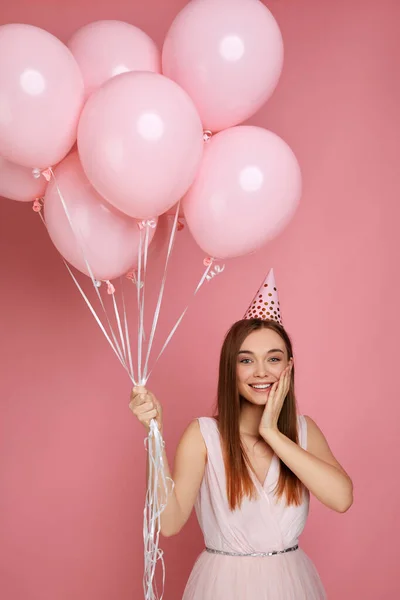 Mujer en sombrero de cumpleaños celebrando con globos de aire de color rosa pastel — Foto de Stock