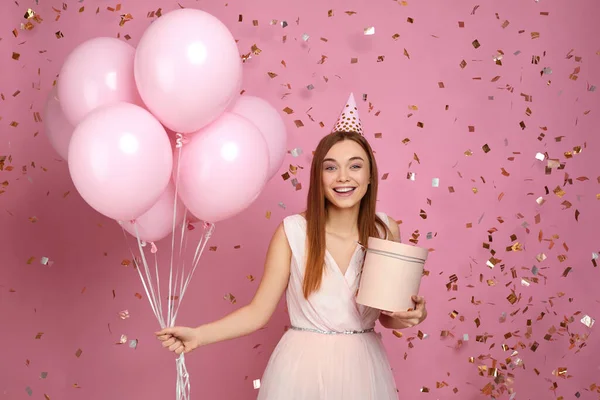 Žena drží dárkové krabice a balónky a padající konfety na růžovém pozadí. — Stock fotografie