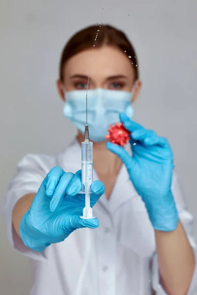 Kvinnlig läkare i mask och gummihandskar med spruta och virusmodell — Stockfoto