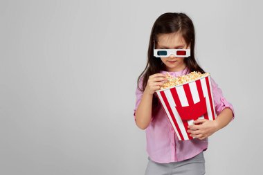 Kırmızı-mavi gözlük takan ve patlamış mısır yiyen çocuk.