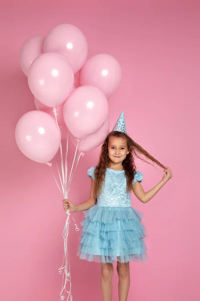 Маленька дівчинка в сукні та капелюсі на день народження святкування з пастельними рожевими повітряними кулями — стокове фото
