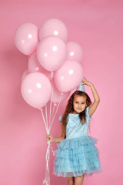 Liten barn flicka i klänning och födelsedag hatt firar med pastell rosa luft ballonger — Stockfoto