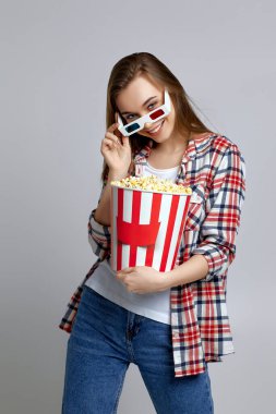 Kırmızı-mavi gözlüklü gülümseyen kadın elinde patlamış mısır kovası tutuyor.