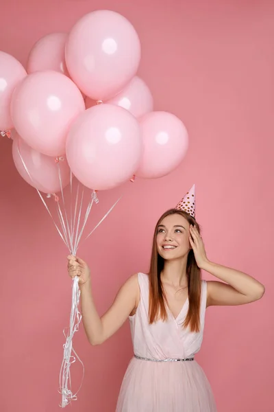 Mujer en sombrero de cumpleaños celebrando con globos de aire de color rosa pastel — Foto de Stock