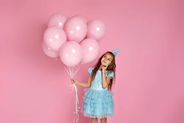 Klein kind meisje in jurk en verjaardagshoed vieren met pastel roze luchtballonnen — Stockfoto