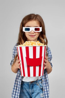 Kırmızı-mavi gözlüklü kız elinde patlamış mısır kovası tutuyor.