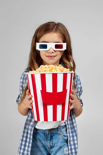 Kırmızı-mavi gözlüklü kız elinde patlamış mısır kovası tutuyor.