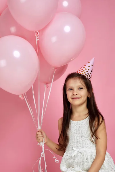 Klein kind meisje in jurk en verjaardagshoed vieren met pastel roze luchtballonnen — Stockfoto