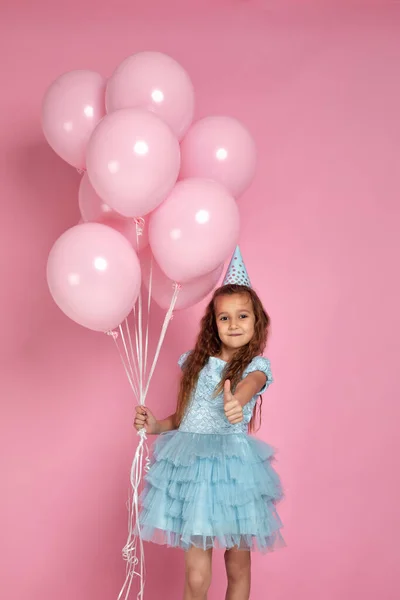 Liten barn flicka i blå klänning och födelsedag hatt med pastell rosa luft ballonger — Stockfoto