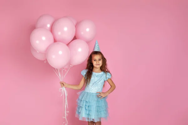 Klein kind meisje in jurk en verjaardagshoed vieren met pastel roze luchtballonnen — Stockfoto