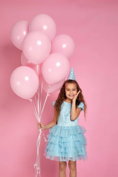 Liten barn flicka i klänning och födelsedag hatt firar med pastell rosa luft ballonger — Stockfoto
